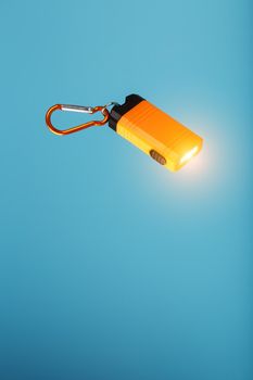 An orange led flashlight with a carabiner glows on a blue background. Led lights in flight. Free space for text. Concept