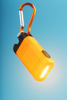 Orange led Flashlight with a carabiner on a blue background. LED lights in flight. Free space for text. Concept