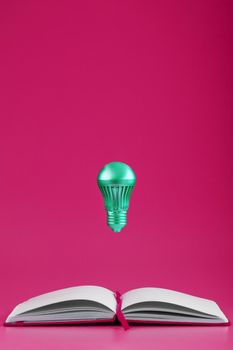 The light bulb hovers over the open pages of an empty notebook on a pink background. Minimalistic style with conceptual ideas. Write down your insights in a notebook.