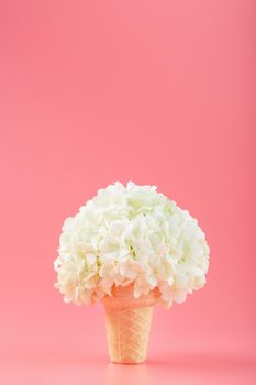 A bouquet of white flowers in an ice cream cone on a pink background. Minimal concept.