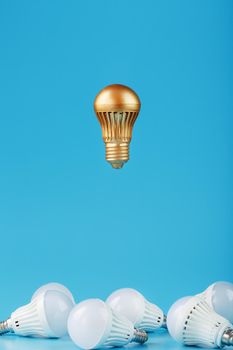 A prominent gold light bulb levitates above an environment of white led bulbs. The concept of an unusual idea and the contrast of surrounding rivals. Minimalism.