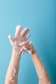 Children's hands in soap suds, on a blue background close-up, top view. Minimalistic concept of free space.