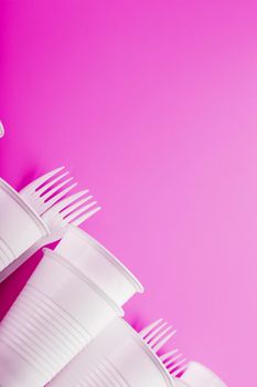 Disposable white plastic tableware on a pink background. Forks and glasses the Concept of a safe environment, ecology. Free space, top view