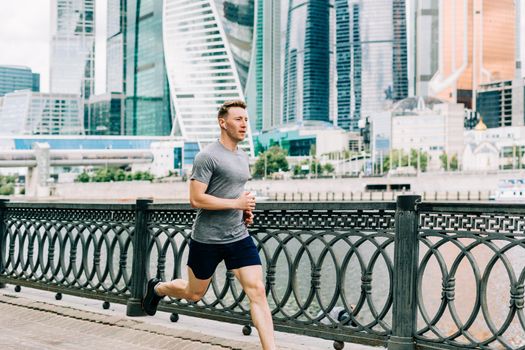 Young athlete man runner running at summer morning, background urban city street. Sports training. Fitness cardio workout in fresh air, jogging outside.