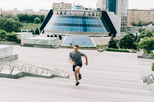 Young athlete man runner running up and down on city stairs in summer on morning run, background urban city street. Sports training. Fitness cardio workout in fresh air, walk outside.