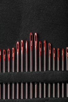 Sewing needles of different sizes in a set of red on a black background. Macro