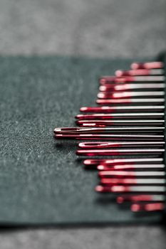 Sewing needles of different sizes in a set of red on a black background. Macro