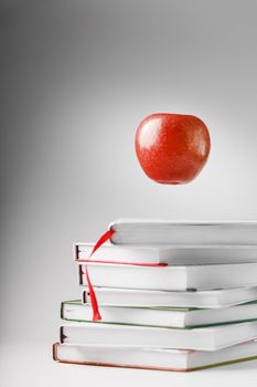A red Apple hovers over a stack of books on a light background. Concept of education and training.