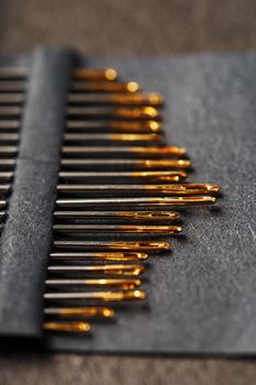 Sewing needles on a black background in a row. Gold eyelets