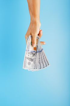 A hand with one hundred-dollar bills on a blue background. The concept of financial assistance. Free space