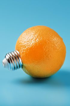 Orange light bulb on a blue background. The orange fruit with base from the bulb E27. The concept of fruit ideas