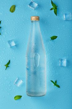 Bottle with an ice cold beverage, ice cubes, drops and mint leaves on a blue background.