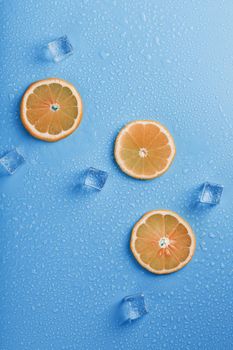 Slices of fresh orange on a blue background with ice. Refreshing cocktail in the summer heat