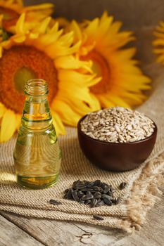 Sunflower oil in a bottle with sunflower seeds and flowers on a wooden background. Composition in the village style. The concept of a bio-organic product. The vertical composition.