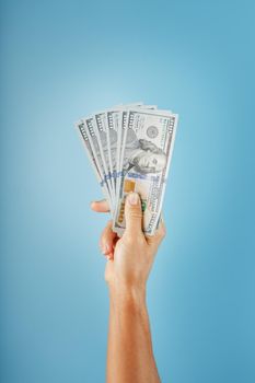 A hand with one hundred-dollar bills on a blue background. The concept of financial assistance. Free space