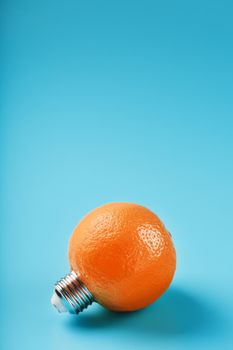 Orange light bulb on a blue background. The orange fruit with base from the bulb E27. The concept of fruit ideas