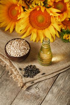 Sunflower oil in a bottle with sunflower seeds and flowers on a wooden background. Composition in the village style. The concept of a bio-organic product. The vertical composition.