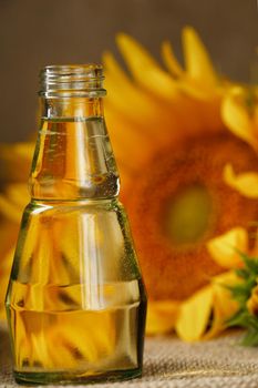 Sunflower oil in a glass bottle and flowers on a wooden background, close-up. Composition in the village style. The concept of a bio-organic product. The vertical composition.