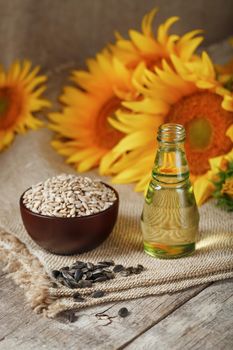 Sunflower oil in a bottle with sunflower seeds and flowers on a wooden background. Composition in the village style. The concept of a bio-organic product. The vertical composition.