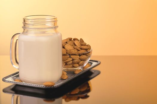 Almond milk in mug jar on yellow background with almonds.