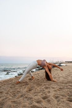 Young woman doing yoga at the beach. Female practices the wild thing yoga pose at sunset. Copy space. Vertical image. Spirituality and healthy lifestyle concepts.