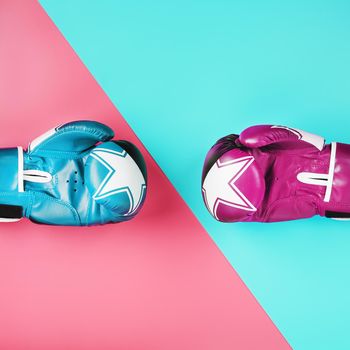 A pair of blue and pink boxing gloves on a blue and pink background. The concept of overcoming difficulties. Feminism, the struggle for the diversity of women's personal and social rights.