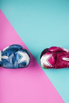 A pair of blue and pink boxing gloves on a blue and pink background. The concept of overcoming difficulties. Feminism, the struggle for the diversity of women's personal and social rights.