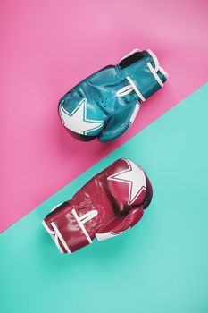 A pair of blue and pink boxing gloves on a blue and pink background. The concept of overcoming difficulties. Feminism, the struggle for the diversity of women's personal and social rights.