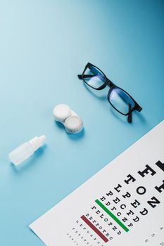 Glasses with Contact Lenses, drops and an Optometrist's Eye Test Chart On a Blue Background. The View From The Top. Free space