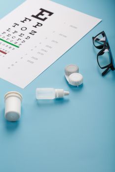 Ophthalmic Accessories Glasses and lenses with an Eye Test Chart for vision correction on a blue background. Treating vision problems. Top view, free space