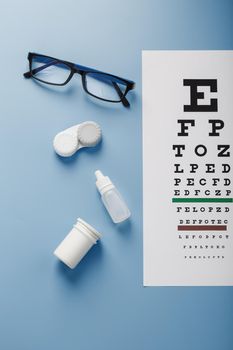 Glasses with Contact Lenses, drops and an Optometrist's Eye Test Chart On a Blue Background. The View From The Top. Free space