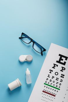 Ophthalmic Accessories Glasses and lenses with an Eye Test Chart for vision correction on a blue background. Treating vision problems. Top view, free space