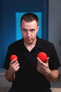 Attractive Caucasian young male masseur holding two massage balls in his hands and looking into the camera. Choice of instruments for self-massage.