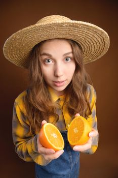 Surprised young woman looks at the camera and holds a cut orange in her hands. Healthy food and fruits in the diet.