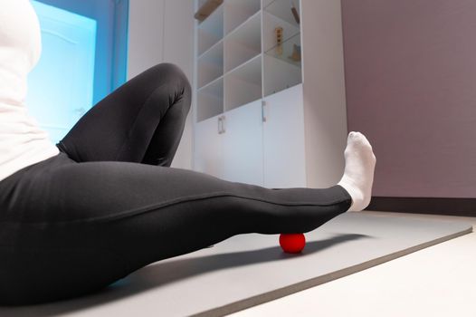 Close-up of self-massage of a sports woman indoors using a massage ball. Myofascial massage without a masseur. Elimination of pain in leg muscles.