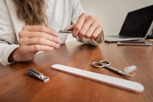 Young caucasian beautiful woman is sitting on a chair in the kitchen at home, busy with her beauty routine, tidies up and beauty her nails on her hands during a manicure. Parallel camera movement on the slider