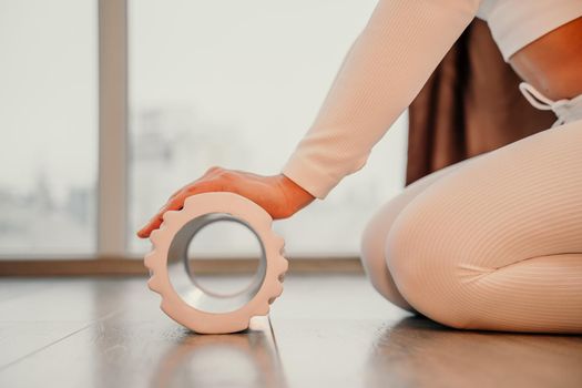 Adult athletic woman, in white bodysuit, performing fascia exercises on the floor - caucasian woman using a massage foam roller - a tool to relieve tension in the back and relieve muscle pain - the concept of physiotherapy and stretching training.