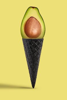 Half a ripe avocado with pit in sweet black waffle cone over beige background. Concept of healthy nutrition, food, seasonal harvest of vegetables and fruits. Close up, copy space