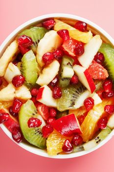 Fruit salad in a white cup on a pink background, free space for text. Slices of fresh, juicy and healthy fruits for a healthy diet.