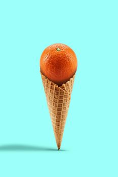 Ripe whole orange in a sweet wafer cone against turquoise background. Concept of healthy nutrition, food and seasonal harvest of fruits. Close up, copy space