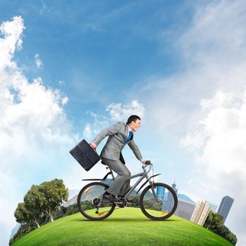 Young man riding bicycle on green field. Businessman on bike hurry to work. Corporate employee wearing business suit with suitcase on cycle outdoors. Cyclist on world round panorama of modern downtown