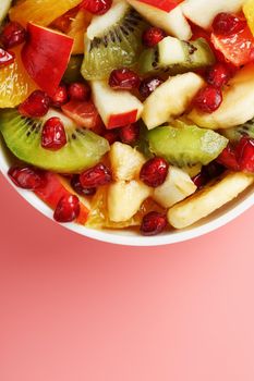 Salad of different juicy ripe fruits in a white cup on a pink background. Free space