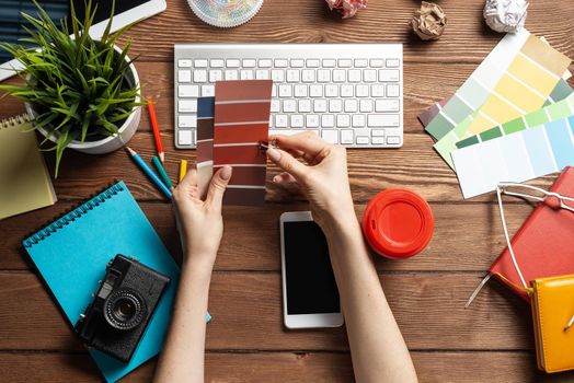 Web designer choosing colors from swatches at wooden desk. Top view office workplace with computer keyboard and stationery. Designing user interface of mobile application. Coloristics in visual design