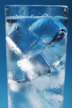 Ice cubes in a misted glass with drops of ice water close-up macro. Refreshing and chilling drink in hot weather. Blue background. Full screen