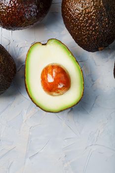 Avocado halves with whole Hass fruits on a background of gray concrete, stone or slate. Top view with copy space.