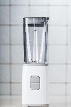 Empty electric blender in the kitchen for cocktails and healthy food. White blender on the table with light kitchen tiles. Minimal concept, copy space.