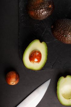 Sliced and whole organic avocado Hass with a knife on a black background. A source of essential fats, vitamins, trace elements, beta-carotene and omega-3 fatty acids.