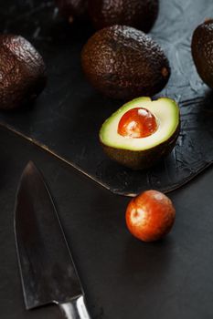 Ripe avocados in a basket on a black table, with a cut fruit and a stone. Free space, top view