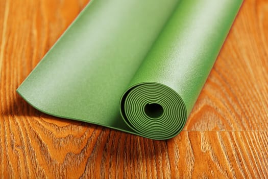 A green yoga mat is laid out in a roll on the wooden floor. A healthy lifestyle in isolation.