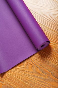 A lilac yoga mat is twisted on the wooden floor. Healthy lifestyle, sports